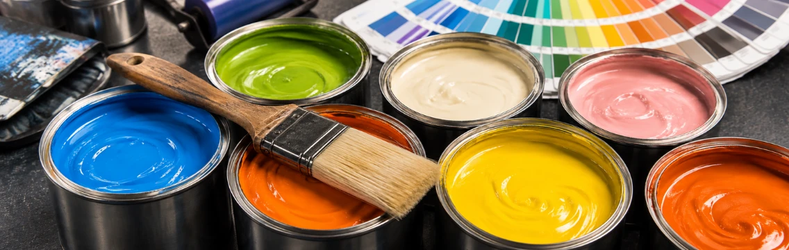 Open tins of coloured paint with a brush and a colour fan, the finishes Molkem driers are formulated for