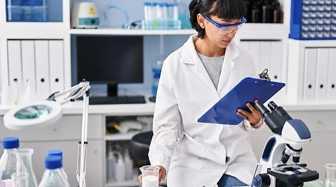 Research scientist recording observations beside a microscope and sample vials during early-stage laboratory work