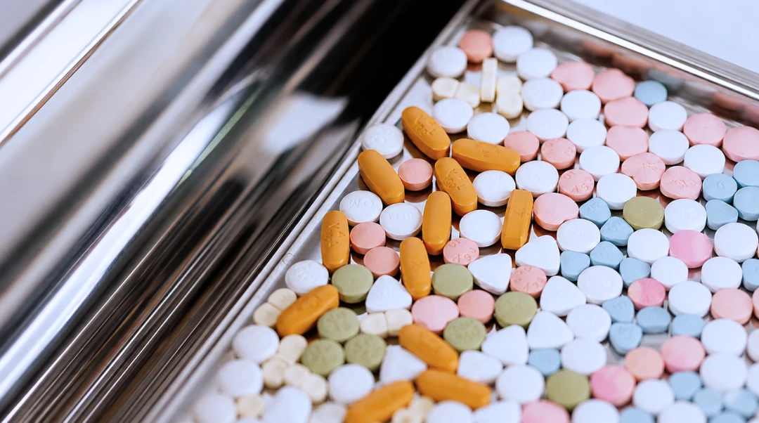 Coloured pharmaceutical tablets and capsules on a stainless steel tray during production